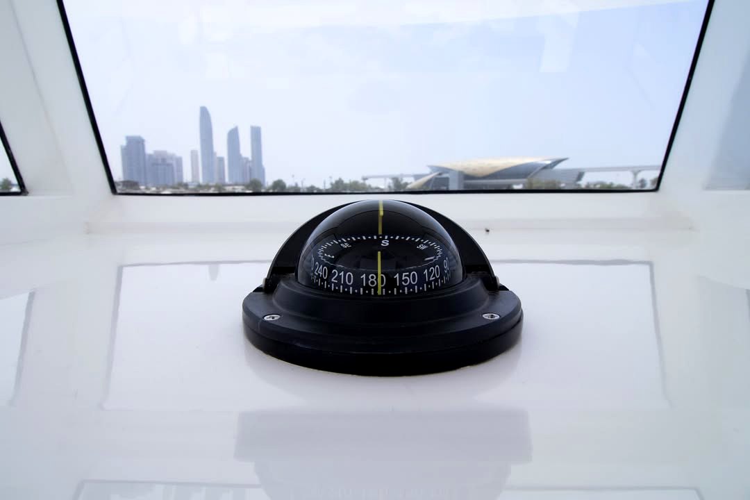 Boat compass with Abu Dhabi skyline through the windshield