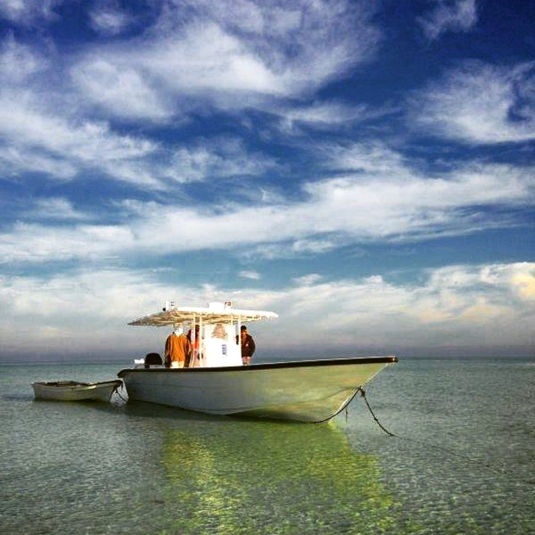 Boat anchored in shallow turquoise Gulf waters under dramatic sky
