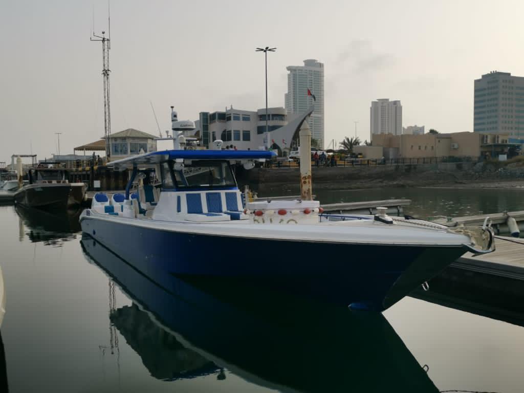 Blue commercial crew boat with covered passenger seating berthed at a harbour at dusk