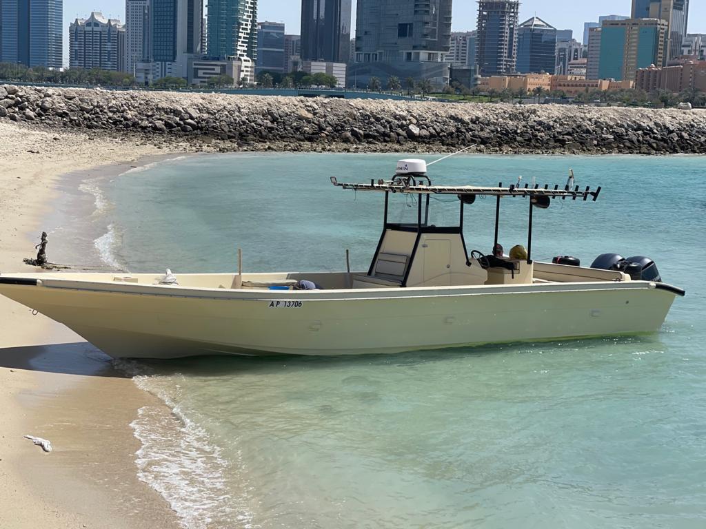 Cream traditional fishing boat anchored off the beach with the Abu Dhabi corniche skyline behind