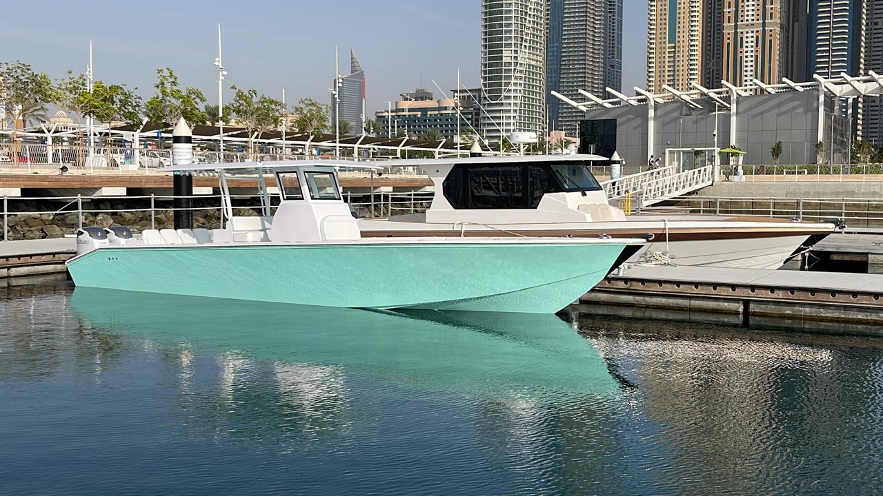 Mint-hulled center console boat berthed at a Dubai marina with the skyline behind